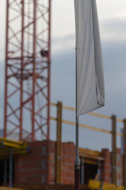 Büyük bir vinç ve beyaz bir bayrağın ön planda bulutlu bir gökyüzüne karşı dalgalandığı bir inşaat alanı..