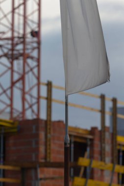 İnşaat alanının arka planında iskele ve vinçlerin olduğu beyaz bayrağın yakın çekimi, bina projelerinde güvenlik ve ilerlemeyi simgeliyor..