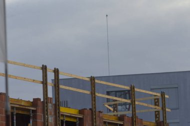 Şehir gelişimini ve inşaat sürecini temsil eden, bulutlu bir gökyüzünün altındaki ahşap iskeleti gösteren bir inşaat sahası..