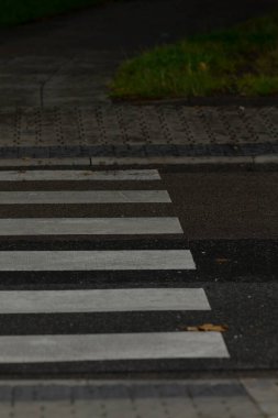Islak yaya geçidinin beyaz çizgili, kentsel yaşamı gösteren yakın plan görüntüsü. Asfalt yağmurdan sonra parlıyor, yayalar için sakin bir atmosfer yaratıyor..