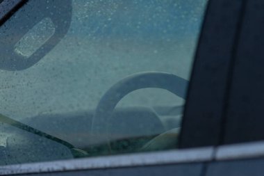 Yağmurlu bir günün özünü ve aracın içini yansıtan, ıslak bir arabanın penceresinden görülen direksiyonun yakın görüntüsü..