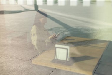 This is a reflection of an individual sitting alone at a table, visible through a glass window, creating an artistic scene