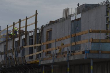 Workers are seen on a construction site, busy framing a new building under cloudy skies, showcasing modern construction techniques and safety measures.