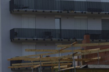 A view of modern apartment balconies with glass railings, juxtaposed against a construction framework in the foreground, showcasing urban development.