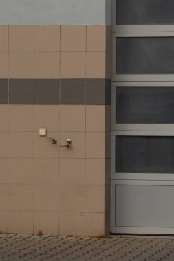 Bir musluk ve modern cam kapı içeren dokulu bir duvarın minimalist görüntüsü. Mimari ve endüstriyel tasarım temaları için ideal.