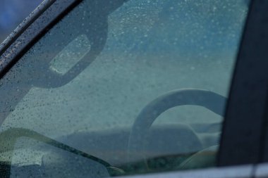 Yağmurdan sırılsıklam olmuş bir pencereden arabanın içini yakından görmek, damlacıkları ve direksiyonu göstermek, yağmurlu bir günün özünü yakalamak..