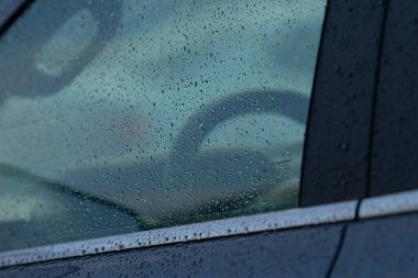 Yağmur damlalarıyla bir arabanın yakın plan görüntüsü, bulanık bir arkaplanda bir direksiyonun yansımasını yakalıyor..