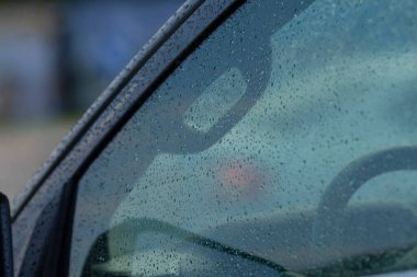 Arabanın ön camındaki yağmur damlalarının yakın plan görüntüsü arkaplan manzarasının bulanık görünmesini sağlıyor. Seyahat ve hava durumu için ideal.