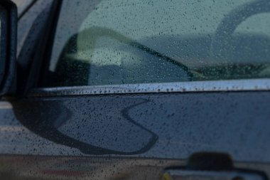 Yağmurun yüzeydeki yansımalarını ve etkilerini gösteren yağmur damlaları olan bir arabanın kapısına yakın plan..