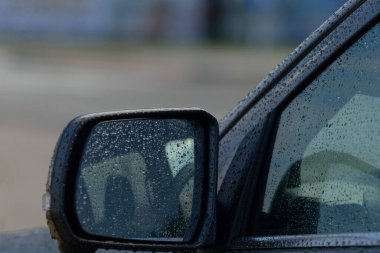 Yağmurlu ortamı yansıtan bir arabanın yan aynası, damlacıklar ve bulanık arka plan, otomotiv ve hava temalı projeler için mükemmel..