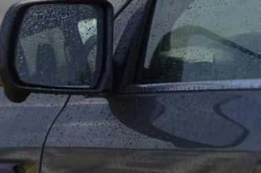 Yağmur damlalarıyla süslenmiş, yağmurlu bir günün özünü yansıtan yan ayna ve kapının yakın plan görüntüsü..