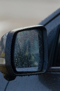 Arka planda bulanık bir görüntü yansıtan yağmur damlaları olan bir arabanın yan aynası. Yağmurlu bir günün havasını yakalar.