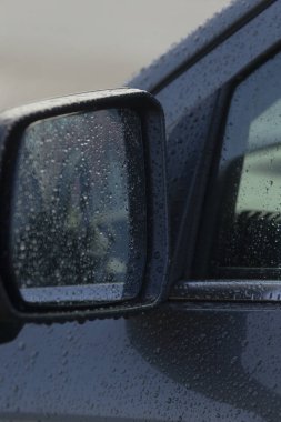 Yağmur damlalarını ve yansımalarını gösteren, yağmurlu bir günün atmosferinin özünü yakalayan bir araba yan aynası..