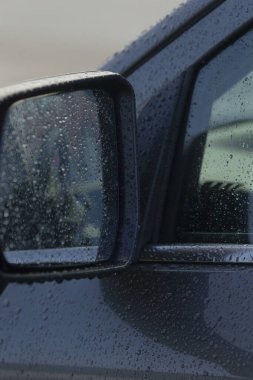 Su damlacıkları ve yansımalarının yer aldığı, yağmurlu bir gün atmosferini gösteren bir araba yan aynası. Otomotiv ve hava temalı görseller için ideal.