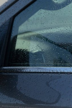 Yağmurdan sırılsıklam olmuş bir arabanın, su damlacıklarını ve yansımalarını gösteren, yağmurlu bir günün özünü yansıtan yakın çekim görüntüsü..