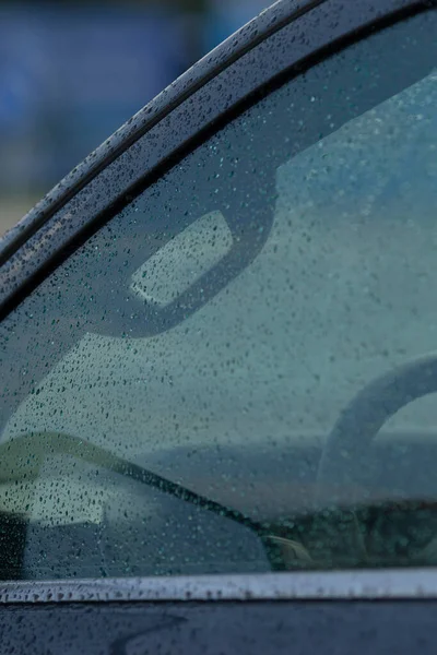 Yağmurdan sırılsıklam olmuş bir arabanın yakın plan çekimi camdaki damlacıkları ve soyut yansımaları sergiliyor ve kasvetli bir atmosfer yaratıyor..