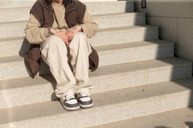 A man is comfortably seated on a set of stairs, his legs crossed in a relaxed manner, enjoying the moment while sitting there
