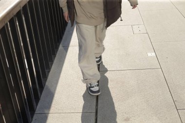 A person casually strolling along a sidewalk while carrying a backpack, enjoying their time outside and taking in the surroundings