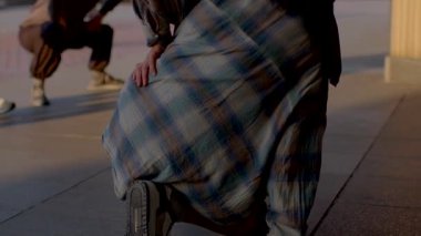 In this urban scene, a diverse group reacts with surprise while covering their ears. A woman in a plaid skirt takes a break nearby