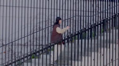 A captivating black and white video depicts a man descending a staircase in front of a grand building, contrasting with women navigating stairs behind a fence