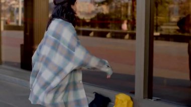 In this lively video, friends chat outside a building. A man smiles while holding a child. Pedestrians include a stylish woman and a man with a yellow backpack