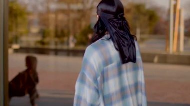 A young woman in a bandana and plaid shirt strolls confidently, while two men chat nearby, embodying the vibrant urban spirit and diverse community