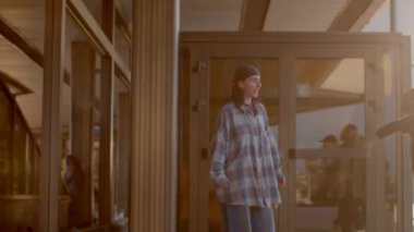 The video depicts a woman and man in plaid shirts in a lively city. The woman walks confidently while the man reflects, showcasing community