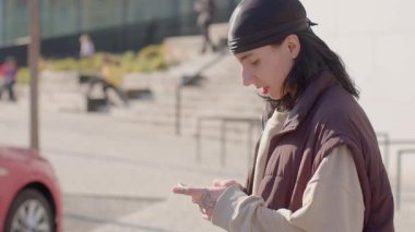 In an urban scene, a man and woman with bandanas interact with smartphones. The man gestures excitedly, while the woman is absorbed, highlighting themes of communication