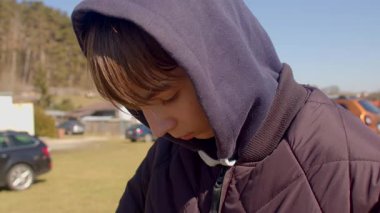 In an expansive field, a contemplative boy and a woman in hooded jackets reflect in solitude. Their serene surroundings evoke connection and introspection