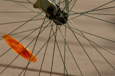 Bisiklet tekeri tellerinin ayrıntılı görüntüsü ve turuncu yansıtıcı güvenlik göstergesi, bisiklet güvenliği ve ekipmanlarını vurguluyor.