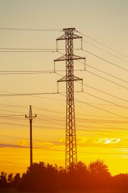 Çarpıcı bir günbatımı, yüksek gerilimli elektrik hatları ve iletişim kulesi için canlı bir zemin oluşturarak ön planda dramatik siluetler oluşturur..