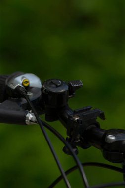 Çan ve çeşitli kablolar içeren bisiklet gidonunun yakın plan görüntüsü bulanık yeşil arka plana karşı, bisiklet sürmenin özünü yakalıyor..