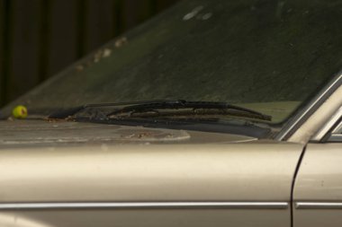 Tozlu cam sileceklerini ve yıpranmış yüzeyini gösteren eski bir aracın yakın çekim görüntüsü. İhmal temaları ve zaman akışı için ideal..