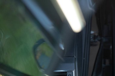 Modern bir arabanın yakın çekim görüntüsü, doğanın yansımaları camda görünür, teknolojinin ve açık havanın karışımını vurguluyor..