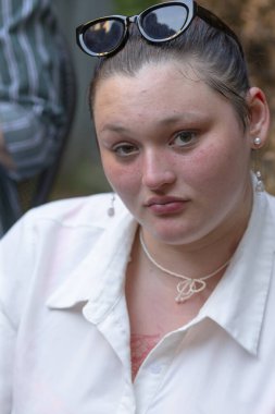A woman who is wearing stylish sunglasses and a beautiful necklace is gazing directly at the camera with a captivating expression