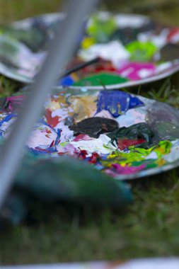 Renklerin değişik renklerinde canlı bir palet boya fırçasının yanındaki yemyeşil çimlerin üzerinde duruyor, yaratıcı çabalar için hazır.