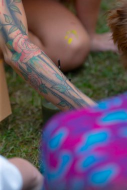 A woman adorned with a beautiful tattoo on her arm is gracefully kneeling on the lush green grass, enjoying the warm summer day