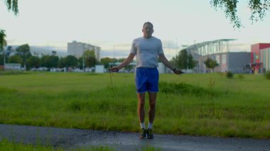 A man jumps rope energetically on a serene park path, surrounded by nature, showcasing fitness, rhythm, and enthusiasm in his workout