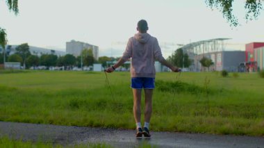 A person is energetically jumping rope in a lush grassy park setting during the early morning hours. The vibrant scene beautifully showcases physical fitness and outdoor exercise in action