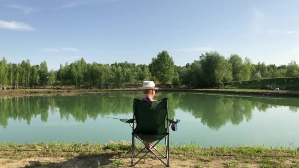 Una ragazza sulla riva del lago siede con una canna da pesca e cattura un pesce. — Video Stock