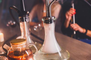 Masada mumlar ve dumanla Nargile manzarası arka planda sigara içen gençlerle nargile salonu, Shisha parti kulübü konsepti.