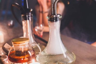 Masada mumlar ve dumanla Nargile manzarası arka planda sigara içen gençlerle nargile salonu, Shisha parti kulübü konsepti.