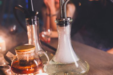 Masada mumlar ve dumanla Nargile manzarası arka planda sigara içen gençlerle nargile salonu, Shisha parti kulübü konsepti.