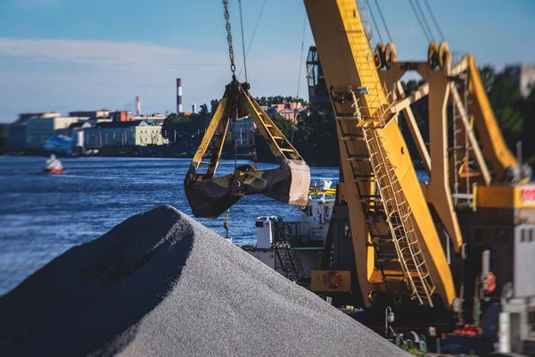 Bulk-handling crane unloading sand, road metal and gravel from cargo vessel ship, heavy vehicle and portal crane loader working with bulk materials in dock terminal