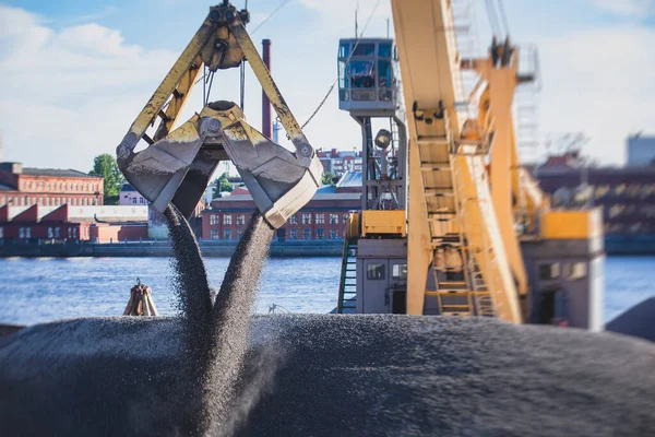 Bulk-handling crane unloading sand, road metal and gravel from cargo vessel ship, heavy vehicle and portal crane loader working with bulk materials in dock terminal