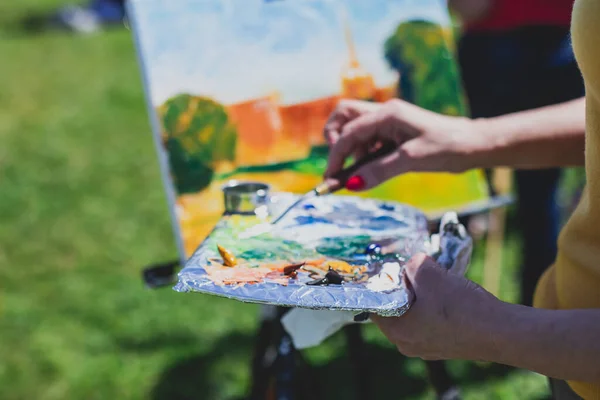 Process of plein air painting, group class of adult talented students in the park with paints easels, and canvases during lesson of watercolour painting outdoors