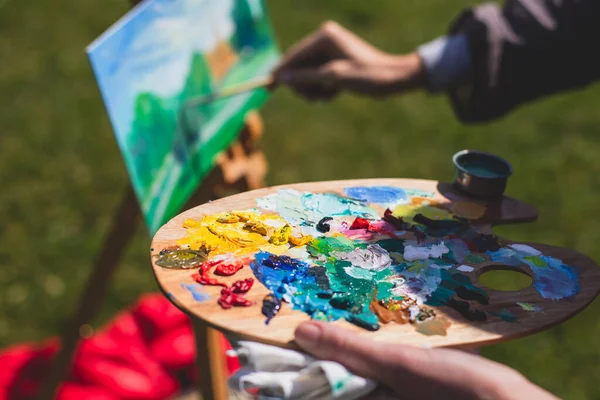 Process of plein air painting, group class of adult talented students in the park with paints easels, and canvases during lesson of watercolour painting outdoors