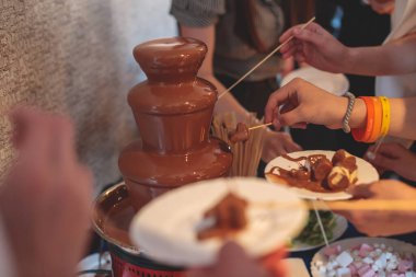 Çikolata Fıskiyesi 'nin canlı resmi bir çocuk doğum günü partisi etrafında çocuklar oynaşıyor ve şekerleme ve meyveleri çeşmeye bandırıyor.