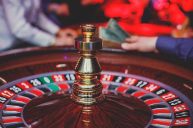 Çok renkli kumarhane masasının canlı bir görüntüsü. Rulet oynanıyor, kumarhane fişleri takılıyor. Krupiye, para ve bir grup zengin kumarbazın eli...