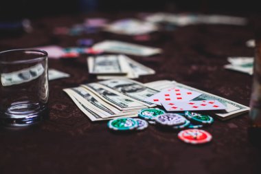 Poker masası, bir deste kart, jeton, alkol, dolar parası ve poker oynayan zengin insanlar.